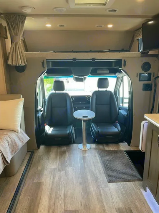 Spacious RV rental interior with cockpit, small table, bed, and overhead bunk.. Forest River Dynamax Isata 3 24FW 2023