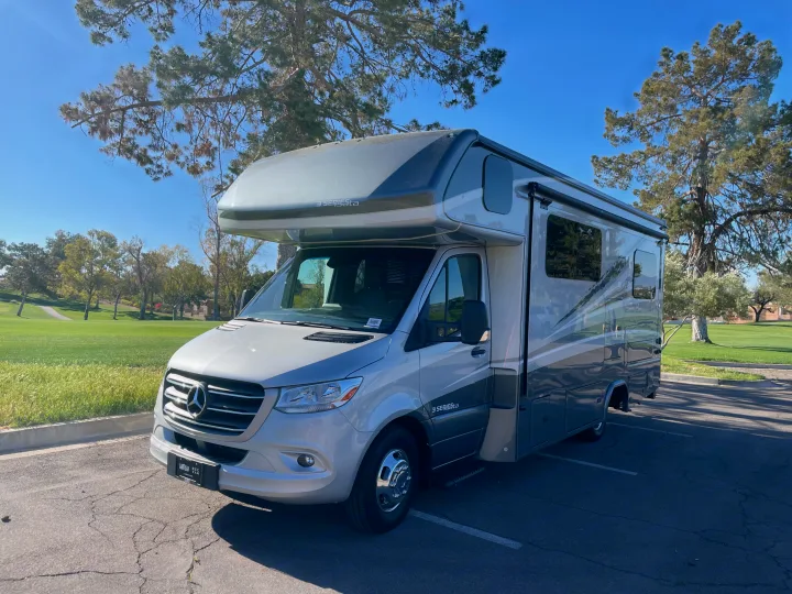 Modern gray RV rental: a Mercedes-Benz motorhome parked next to a golf course on a sunny day.. Forest River Dynamax Isata 3 24FW 2023