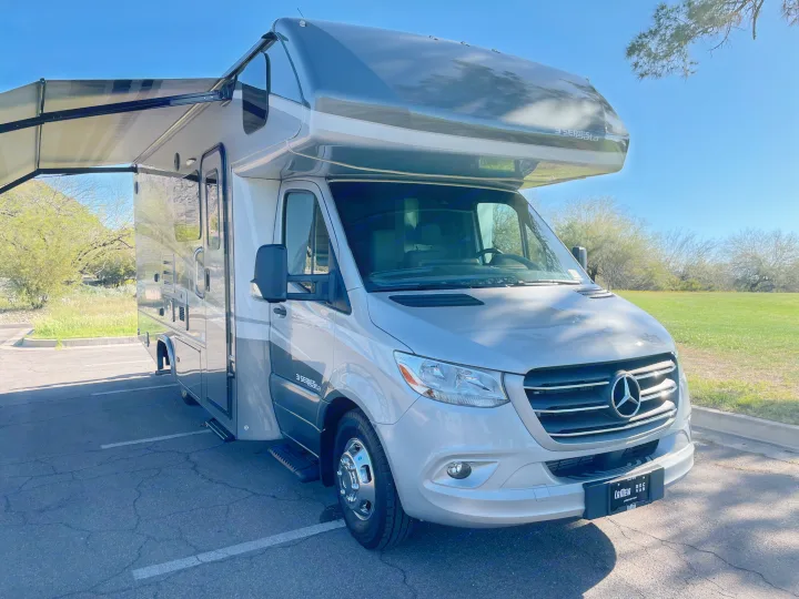 Grey Mercedes-Benz Class C RV rental with an extended awning, parked on asphalt.. Forest River Dynamax Isata 3 24FW 2023