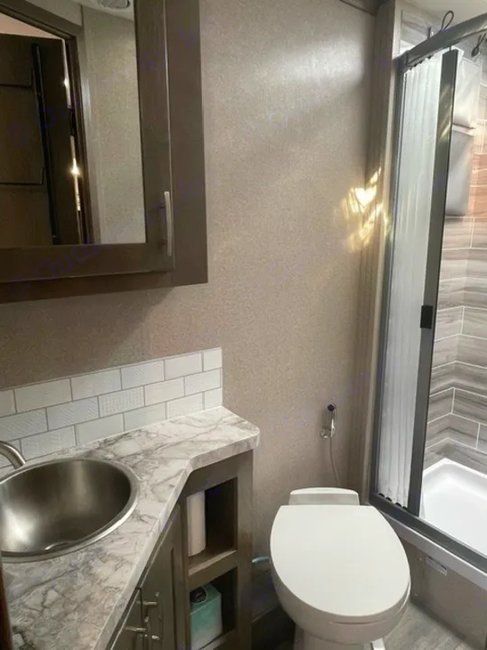 Well-appointed RV rental bathroom featuring a sink, toilet, and glass-enclosed shower. Compact & functional for trips.. Forest River Dynamax Isata 3 24FW 2023