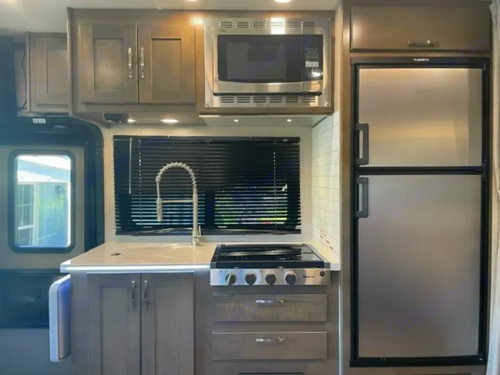 Explore this compact RV rental kitchen, equipped with a sink, stove, microwave, and large refrigerator, set in neutral tones.. Forest River Dynamax Isata 3 24FW 2023