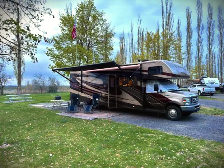 An RV rental is parked at a serene campsite with an extended awning, ready for outdoor relaxation. Perfect for a camping trip.. Forest River 3051S Ford 2017