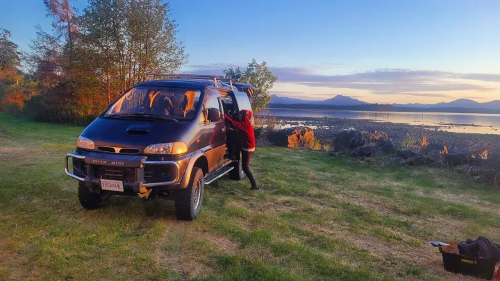 An RV rental campervan offers stunning views of a tranquil lake and mountains, perfect for your next outdoor escape.. MITSUBISHI Delica 1997