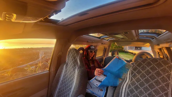 Inside a rental SUV, a person plans their RV rental route, engrossed in a map during sunset by the water.. MITSUBISHI Delica 1997