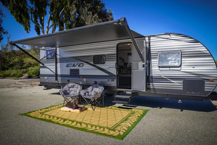 This rv rental shows a travel trailer with an extended awning, outdoor chairs, and a dog on a mat for comfortable outdoor living.. Forest River EVO 2021