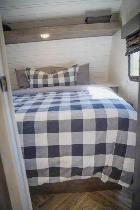 Cozy RV rental bedroom with black & white buffalo plaid bedding, shiplap walls, built-in light & window.. Forest River EVO 2021