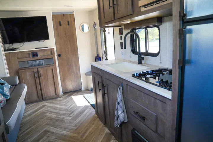 Inside a modern RV rental: well-equipped kitchen with stovetop, sink, and TV area with sofa, ready for your adventure.. Forest River EVO 2021