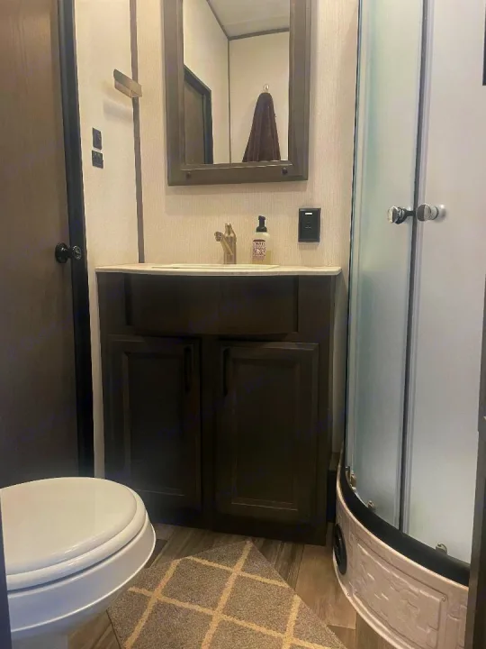 Compact RV rental bathroom with a vanity, toilet, and curved shower, designed for efficient travel.. Heartland 265 2021