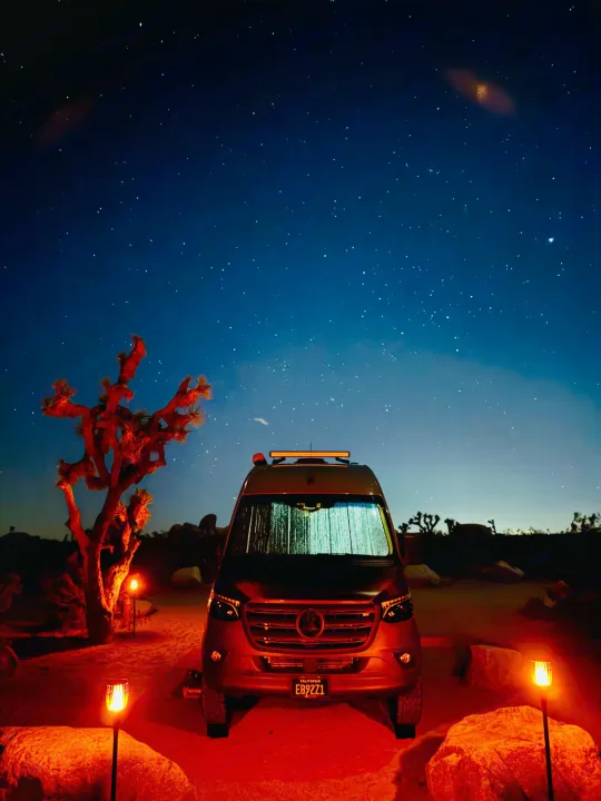 Stargazing adventure with an RV rental: a van under a brilliant starry desert sky, surrounded by Joshua trees and warm lights.. Synergy Mercedes-Benz Sprinter 2022