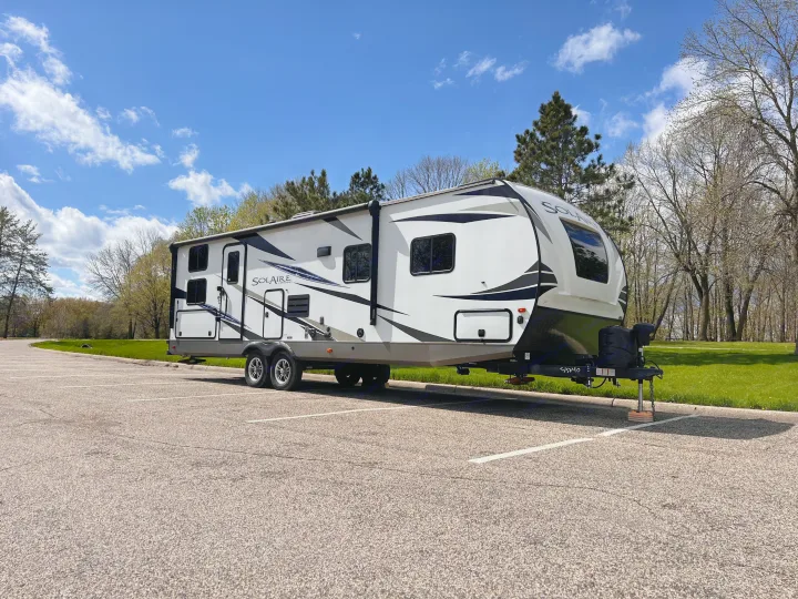 This Solaire travel trailer, available for RV rental, is parked on a sunny day amidst trees.. Forest River Solaire 2020