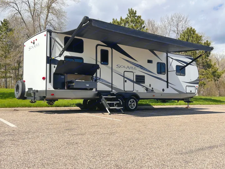 Spacious white SolAire RV rental with extended awning & outdoor kitchen, ready for adventure on a paved lot.. Forest River Solaire 2020