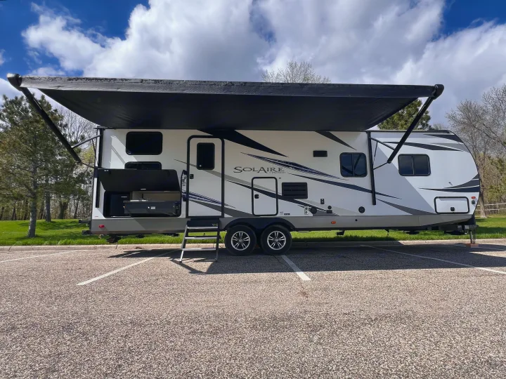 White Solaire travel trailer RV rental with extended awning and outdoor kitchen, parked for sunny camping.. Forest River Solaire 2020