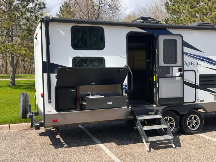 White Solaire RV rental, equipped with an open outdoor kitchen (fridge, sink) and deployed steps. Ready for travel/camping.. Forest River Solaire 2020