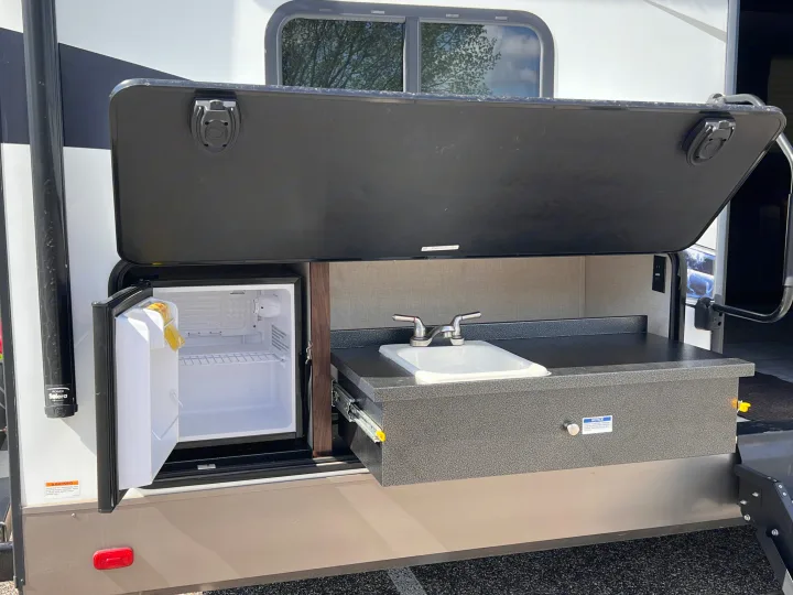 RV rental outdoor kitchen with open mini-fridge, sink & counter under a lift-up hatch.. Forest River Solaire 2020