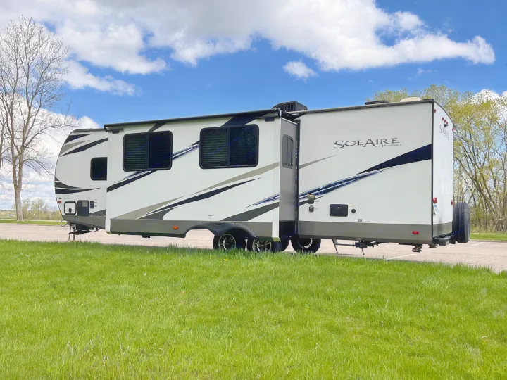 A white Solaire travel trailer with slide-outs extended, perfect for your next RV rental adventure. Parked by green grass.. Forest River Solaire 2020