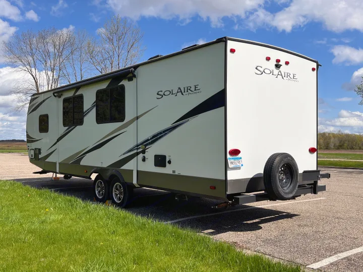 A white SolAire travel trailer RV, a type often seen as an rv rental, is parked on asphalt with green grass and a blue sky.. Forest River Solaire 2020