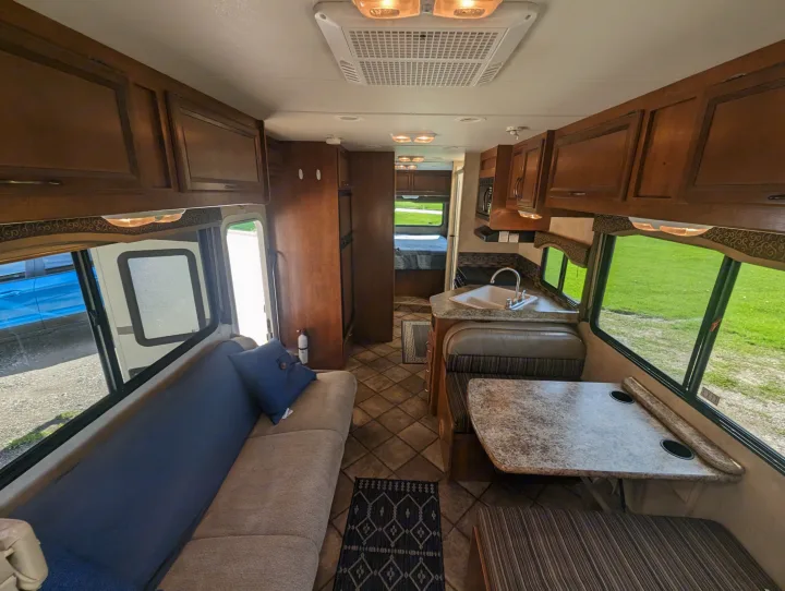 Spacious RV rental interior: living area, dining booth, kitchen, and ample wood cabinetry with scenic outdoor views.. Thor Motor Coach Four Winds 2014
