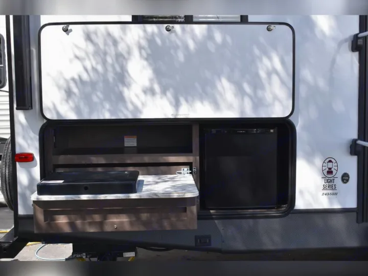 This travel trailer RV rental boasts an outdoor kitchen featuring a mini-fridge, countertop, and pull-out cooktop, perfect for camping.. Dutchmen Coleman Light 2021