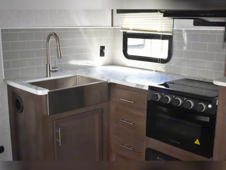 Inside a compact RV rental kitchen: stainless steel sink, sleek black stove/oven, and gray tile backsplash.. Dutchmen Coleman Light 2021