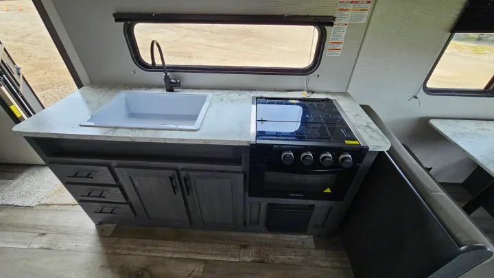 This RV rental's kitchen features a modern sink, Greystone oven/stove, and stylish marble-patterned countertops, ideal for camping.. Aspen Trail LE 2022