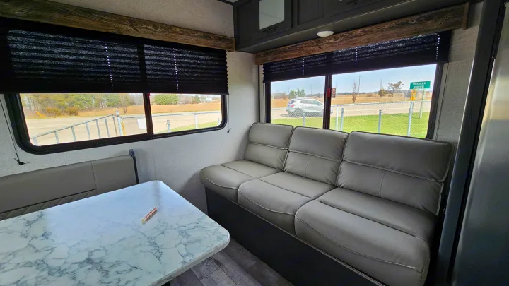 Cozy RV rental interior featuring a grey sofa, dining table, and large windows revealing outdoor scenery.. Aspen Trail LE 2022
