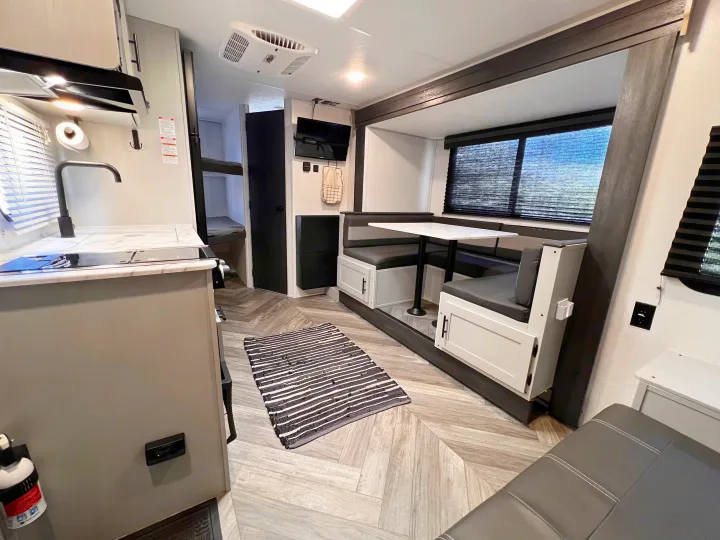 Sleek RV rental interior: kitchen, modern dinette, and bunk beds with herringbone floors.. Wildwood FSX 2021