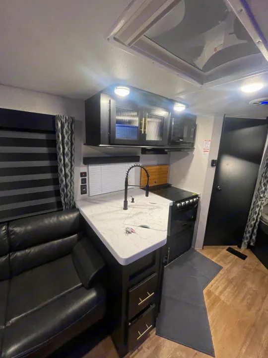Stylish RV rental interior featuring a modern kitchen with black cabinets, white counters, and a comfy black leather sofa.. Forest River Cherokee 2021