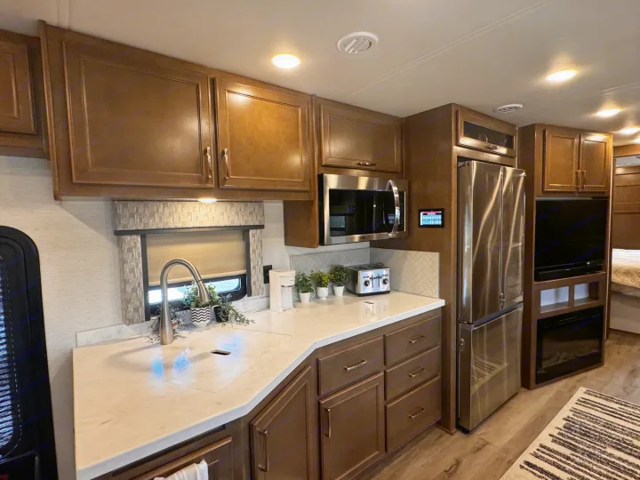 Modern rv rental kitchen featuring rich wood cabinets, stainless appliances, a spacious sink, and inviting living area.. Renegade Verona 40 VRB 2024
