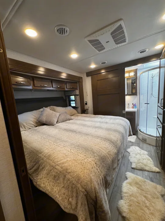 Comfortable RV rental bedroom featuring a large bed, overhead storage, and an attached compact bathroom with shower.. Renegade Verona 40 VRB 2024
