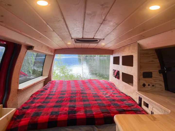 Inside this RV rental: wood-paneled interior, comfy bed with plaid blanket, built-in storage, and a stunning lake view.. Gmc Savanna 2010