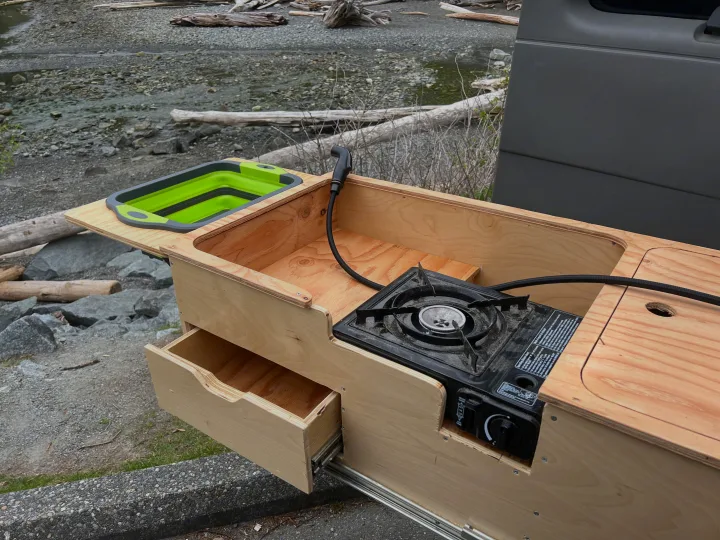This custom RV rental kitchen slides out, featuring a portable stove, sink, and drawer for convenient outdoor cooking by the water.. Gmc Savanna 2010