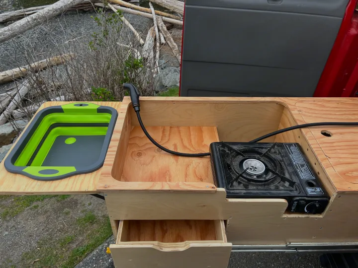 RV rental's pull-out kitchen: A compact setup with collapsible sink, portable stove, and storage drawer.. Gmc Savanna 2010