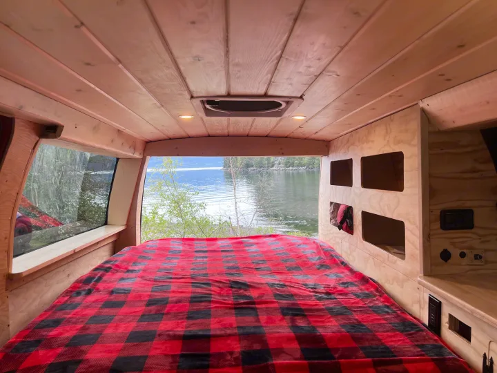 Cozy rv rental interior with a plaid bed and stunning lake view from the large window.. Gmc Savanna 2010