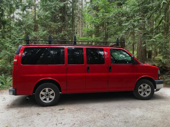 Red van with roof rack in a lush forest setting. Perfect for an RV rental and outdoor adventures!. Gmc Savanna 2010
