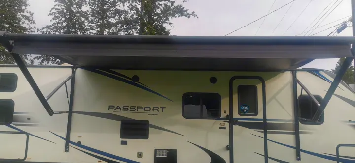 Side view of a white Passport by Keystone RV rental with its black awning extended, ready for outdoor adventures.. Keystone RV Passport 2019