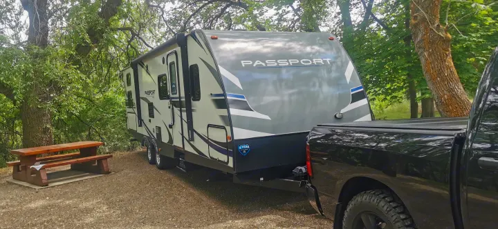 Travel trailer RV rental hooked to truck at a rustic campsite with trees & picnic table.. Keystone RV Passport 2019