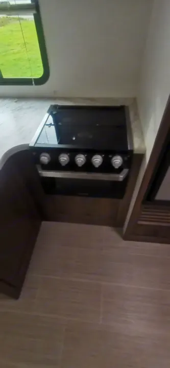 RV rental's compact kitchen: a stovetop, oven, and countertop next to a window view.. Keystone RV Passport 2019