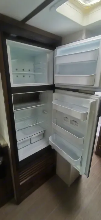 A clean, empty RV rental refrigerator and freezer, ready for your trip, showing shelves, door bins, and crisper drawers.. Keystone RV Passport 2019