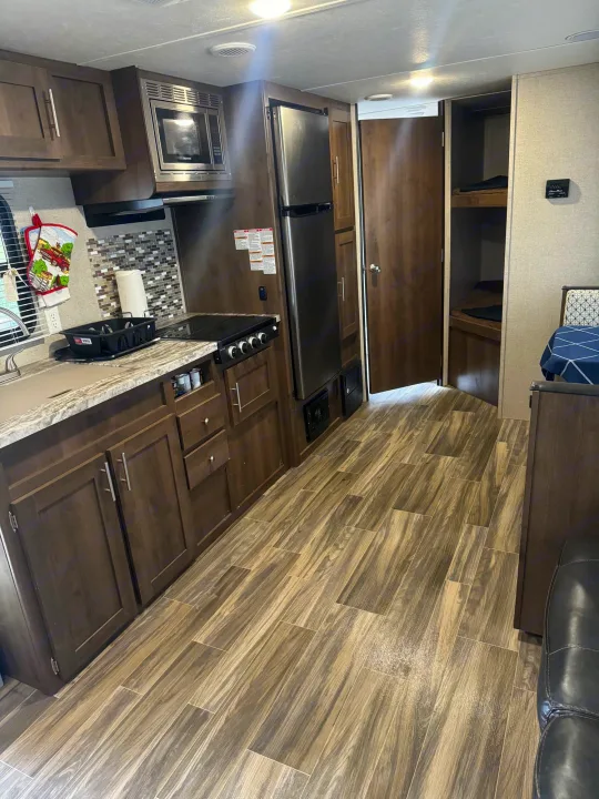 Inside an rv rental: a modern kitchen with microwave, fridge, stove, and sink, leading to bunk beds and living space.. Shasta 26db 2020
