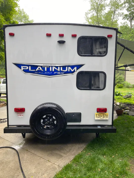 Rainy day at the back of an RV rental. White travel trailer, spare tire, and New Jersey plate, ready for outdoor adventures.. Forest River Salem FSX Plantium 2022