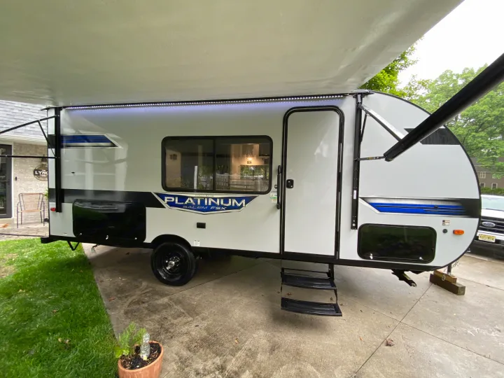 Modern white rv rental travel trailer with extended fabric awning, LED lights, blue accents, and entry steps.. Forest River Salem FSX Plantium 2022