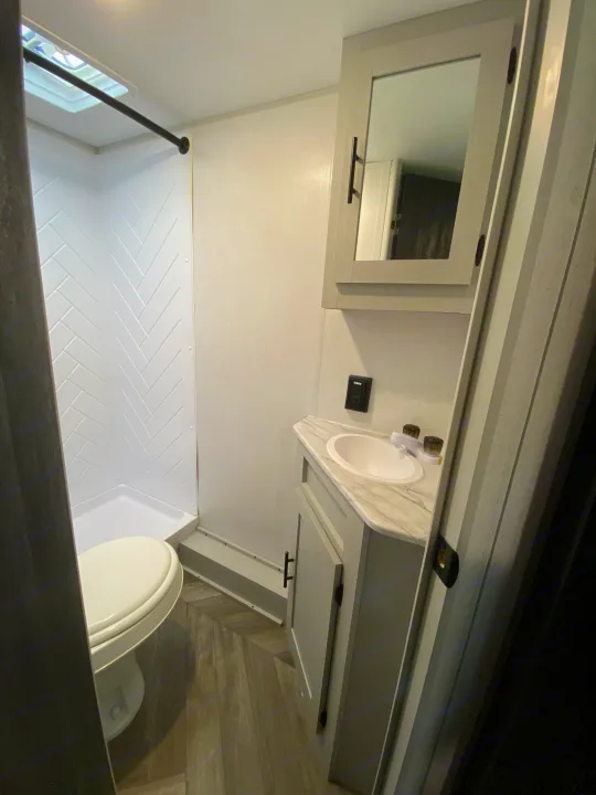 Compact RV rental bathroom with a white shower, toilet, and vanity with sink. A mirrored cabinet is above.. Forest River Salem FSX Plantium 2022