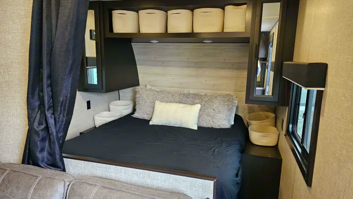 Inside an RV rental: a cozy bedroom with a dark bed, fluffy pillows, overhead baskets, & side window. Ideal for trips.. Jayco Jay Flight Baja Edition 2023