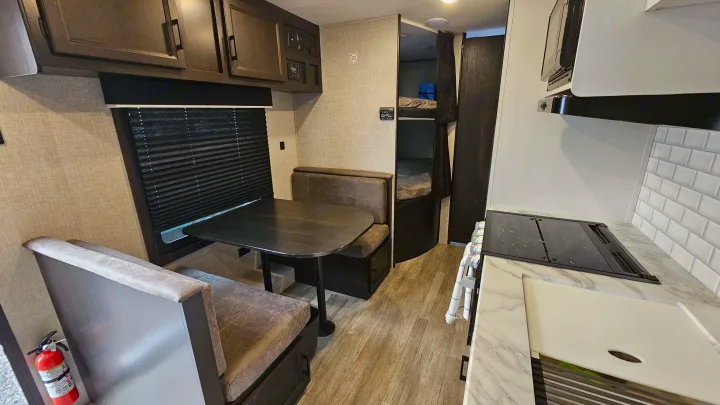 RV rental interior showing a functional dinette, kitchen area, and a glimpse of the bunk bed sleeping space.. Jayco Jay Flight Baja Edition 2023