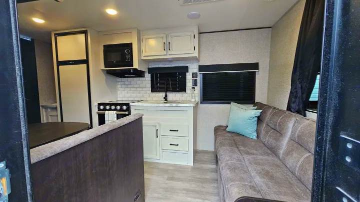 Inside this RV rental: a compact, modern kitchen (fridge, stove, microwave) and a cozy brown sofa.. Jayco Jay Flight Baja Edition 2023