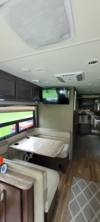 Inside this RV rental, a cozy dining booth with a table faces a wall-mounted TV, with the bedroom visible beyond.. Thor A.C.E. 2017