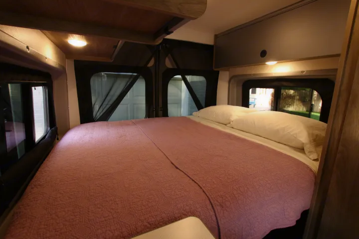 Cozy RV rental bedroom with a large bed, pink quilt, white pillows, and soft lighting, ideal for comfortable travel.. Winnebago Solis 2023