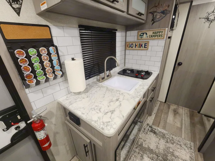This RV rental's compact kitchen galley features a sink, stove, K-cup coffee station, and 'Happy Campers' decor.. Other 17B 2023