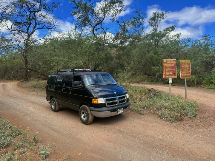 Explore Makena State Park in this black rv rental van on a dirt road. A dog looks out, ready for a Hawaii adventure.. Dodge 1500 1999