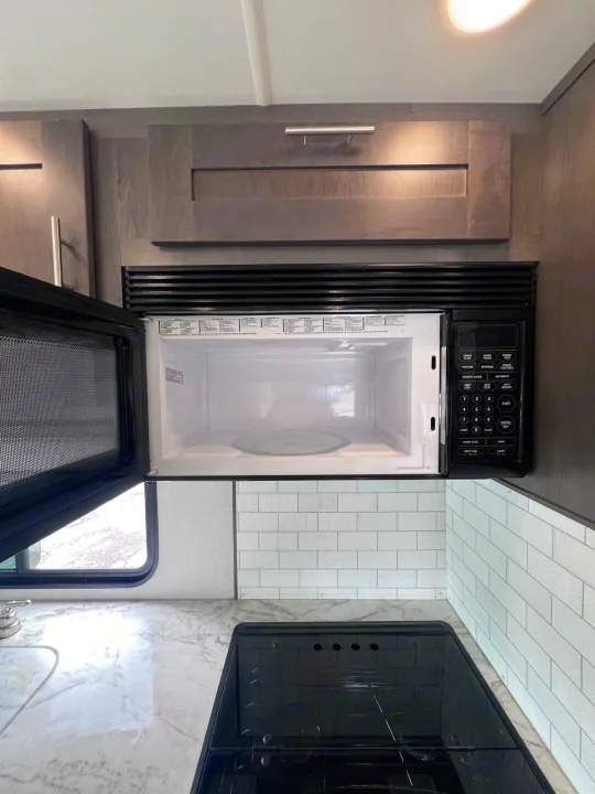 RV rental kitchen featuring an open microwave, black glass stovetop, marble-look counter, and grey wood cabinets.. Forest River Georgetown 2022